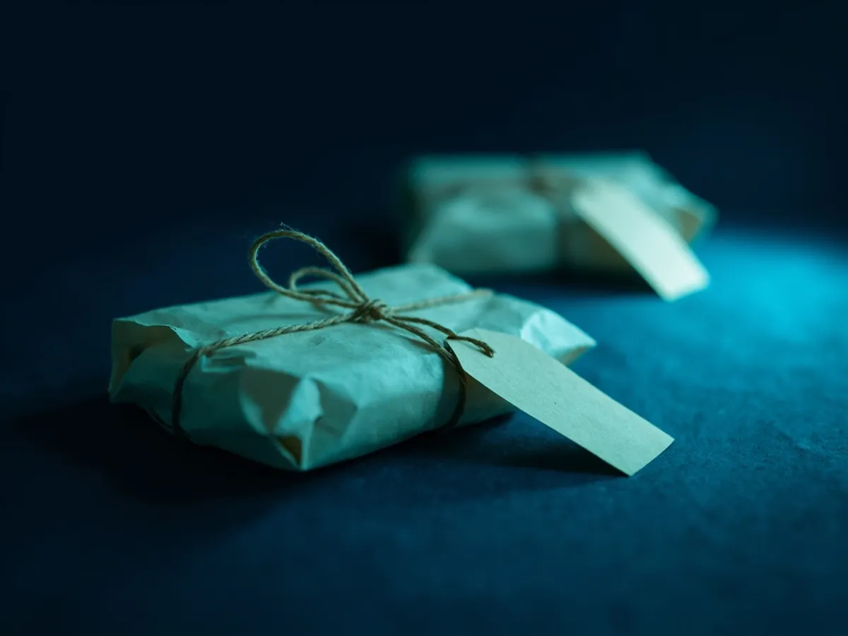 Two identical parcels on a dark table, one with a paper price tag tied with string