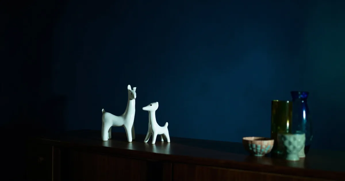 Mid-century porcelain figurines and a coloured glass vase grouped on a dark sideboard