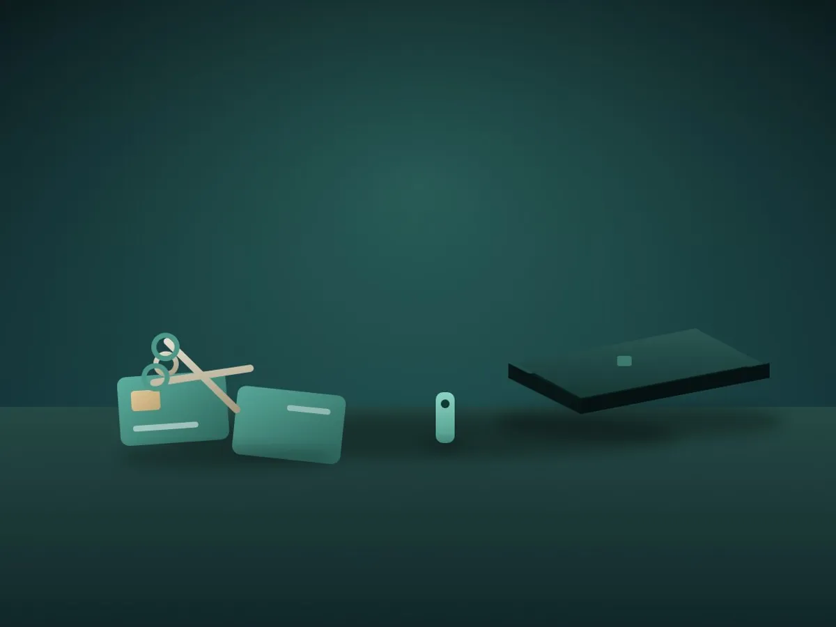 A bank card cut in half with scissors next to a small security key and a closed laptop
